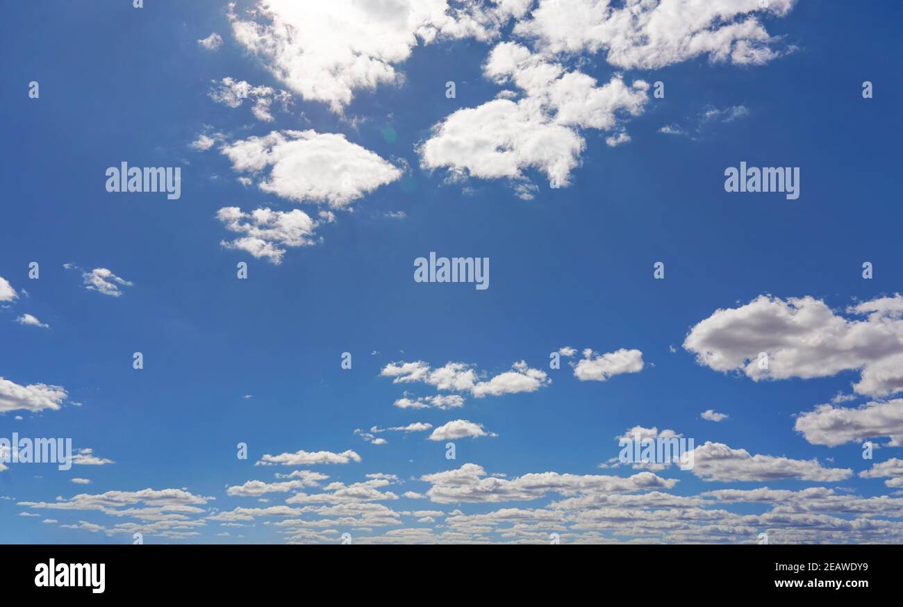 Bright sky background with few small clouds, strong sun shines through creating some lens flares Stock Photo