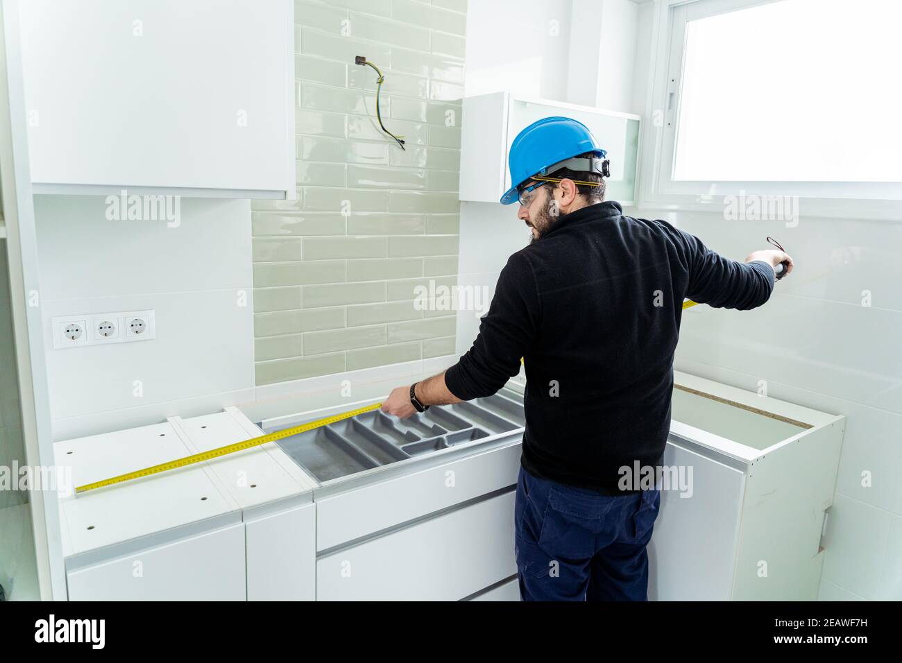 Worker taking measurement of a kitchen that he is assembling Stock Photo