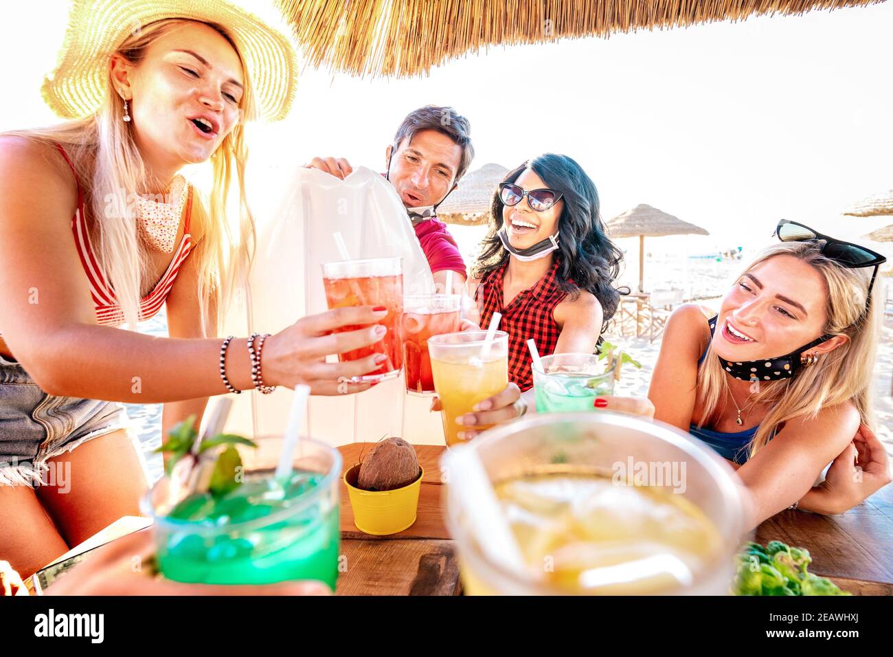 Happy friends drinking at beach cocktail bar wearing face masks - New normal summer concept with people having fun together toasting drinks Stock Photo