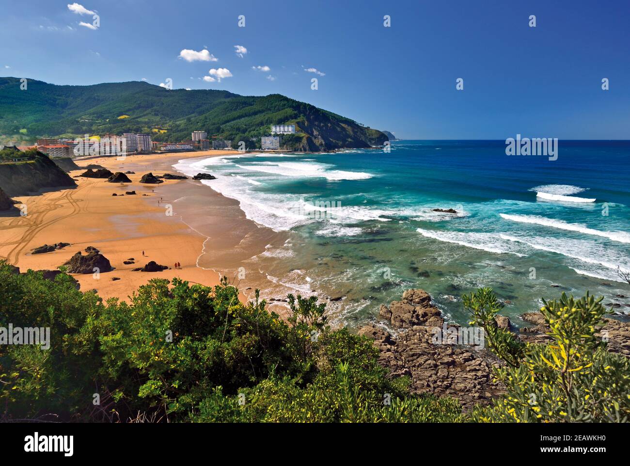 View of sand beach with blue ocean and white waves surrounded by green hills Stock Photo