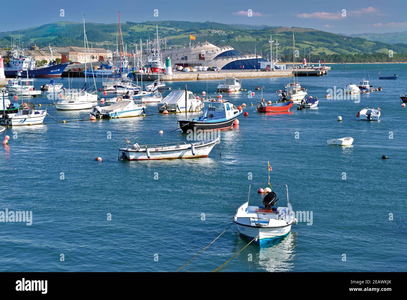 Fishing boats anchoring in harbour with shiplike building and green hills in the background Stock Photo