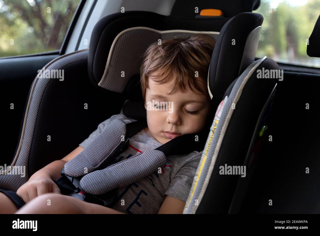 Little boy sleeping on the harness booster seat into a car. Security seat for children. Stock Photo