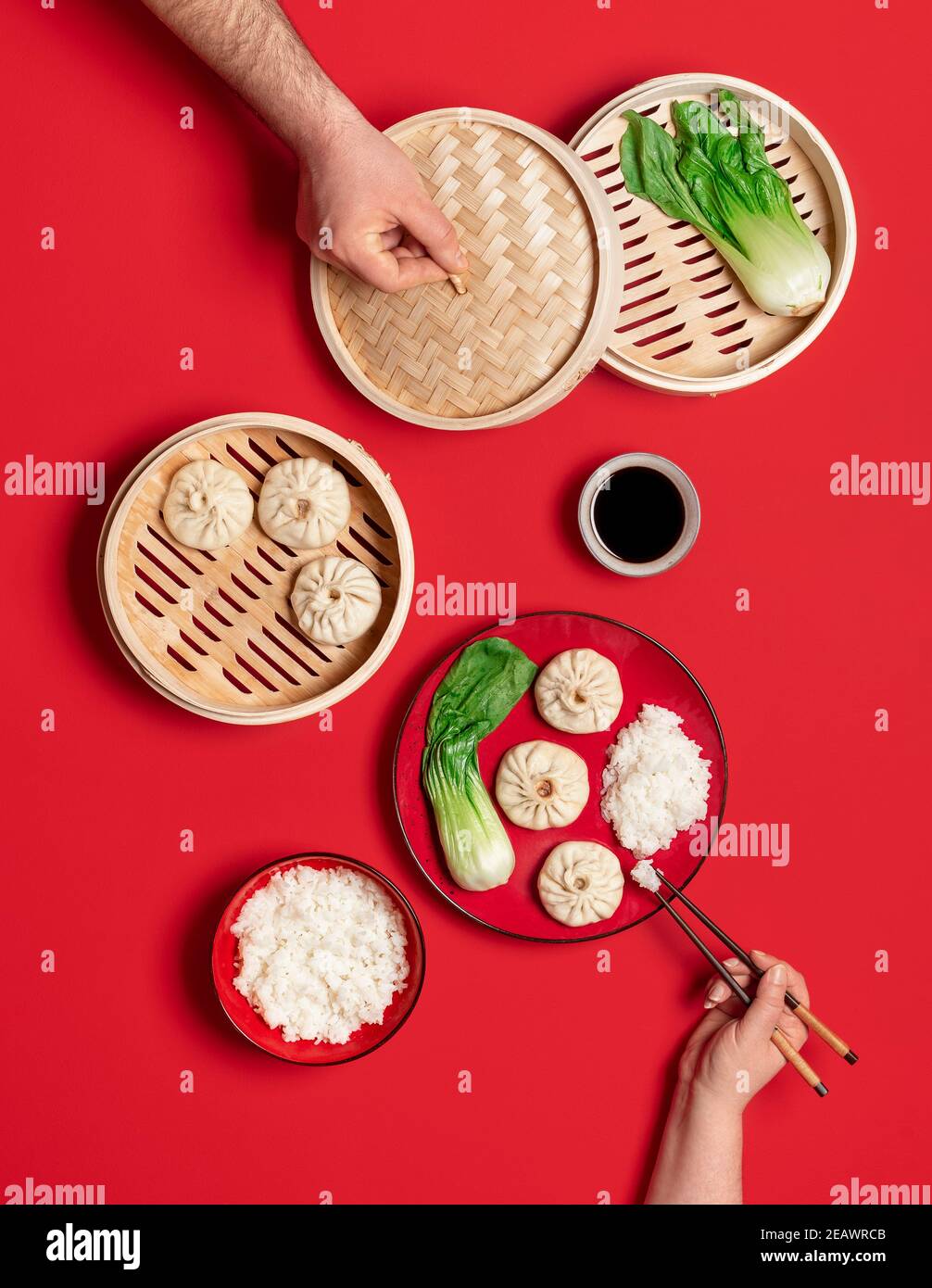 Chinese dinner table with steamed pork baozi dumplings, pak choi, and rice, isolated on a red background. Top view with Chinese Xiao Long Bao buns. Stock Photo