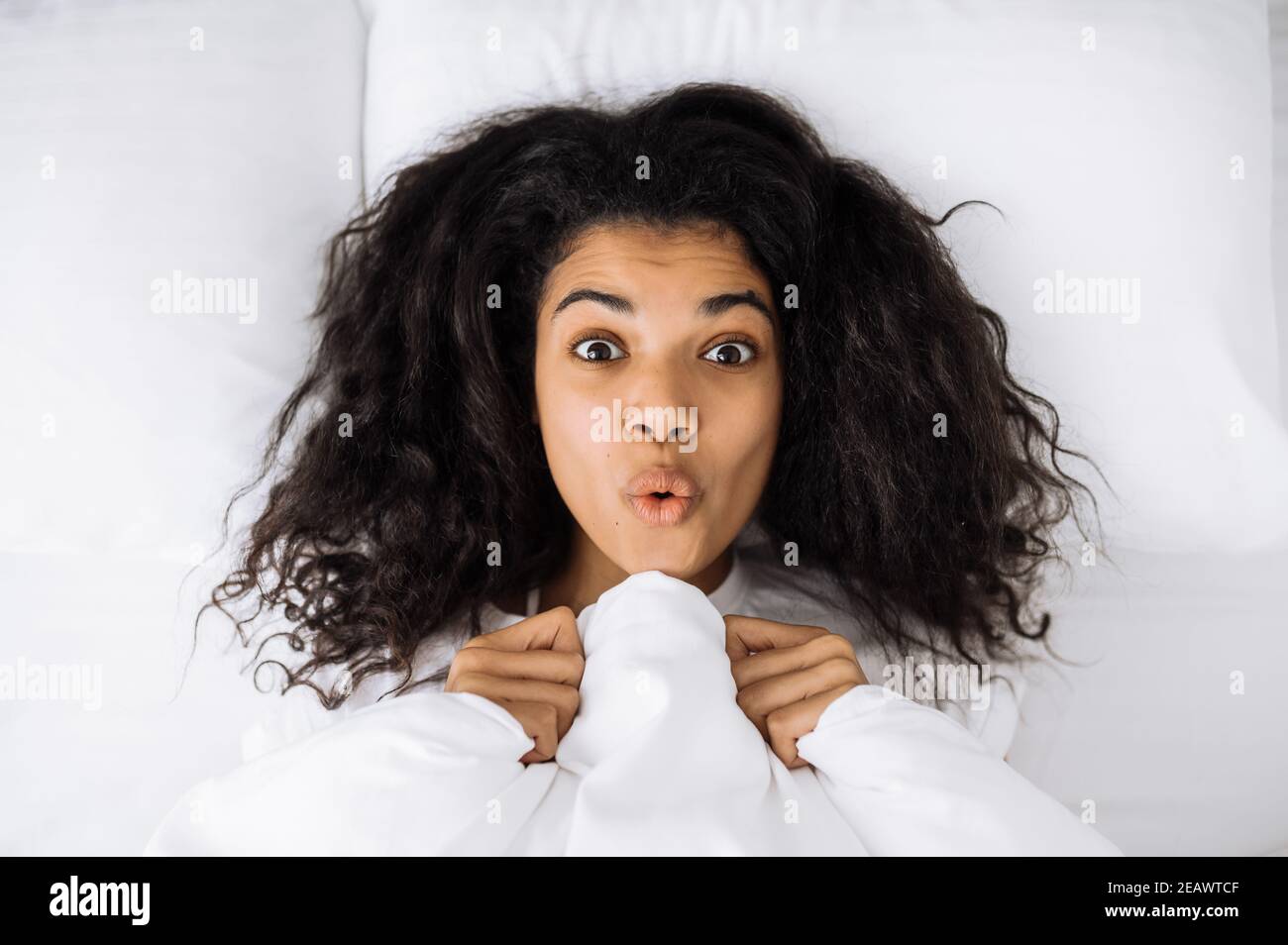 African american young woman lay in bed, posing, making funny faces. Happy female relaxing in bed, after good night sleep. Beautiful girl waking up, f Stock Photo