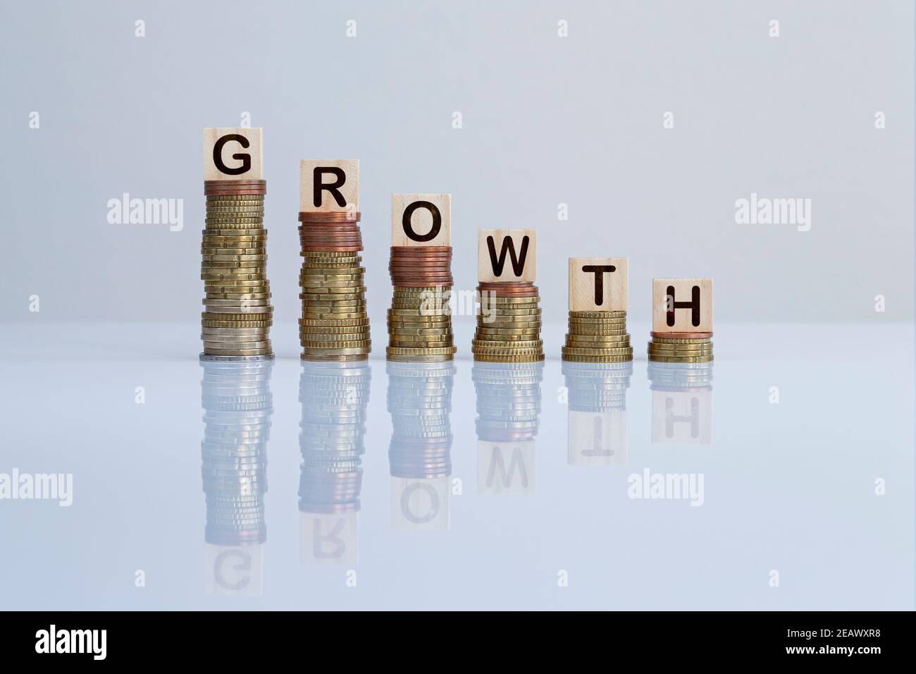 Word 'GROWTH' on wooden blocks on top of descending stacks of coins on gray. Concept photo of economic crisis, recession and financial reduction. Stock Photo