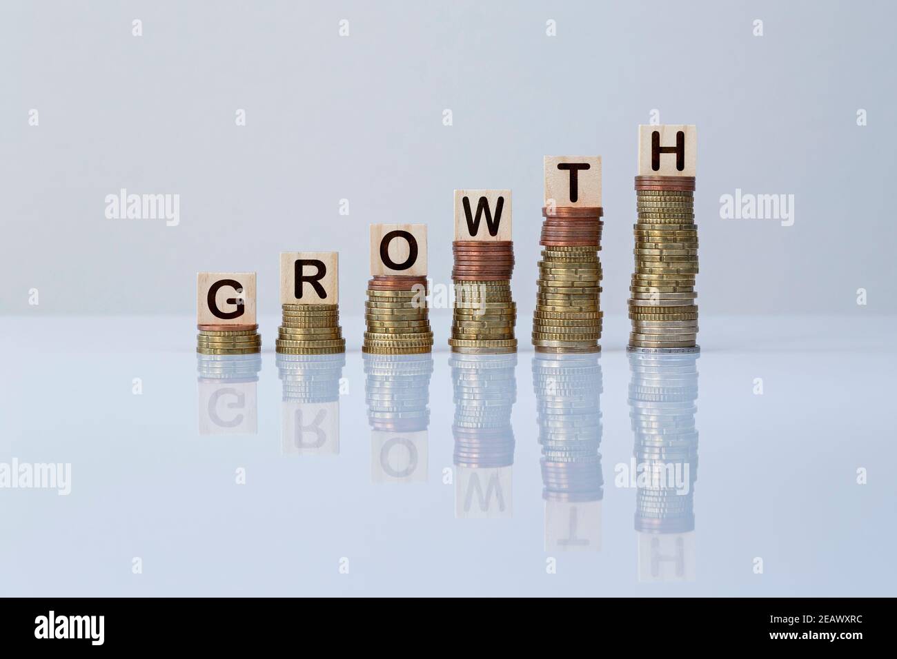 Word 'GROWTH' on wooden blocks on top of ascending stacks of coins on gray background. Concept photo of economy, business, finance, financial growth. Stock Photo