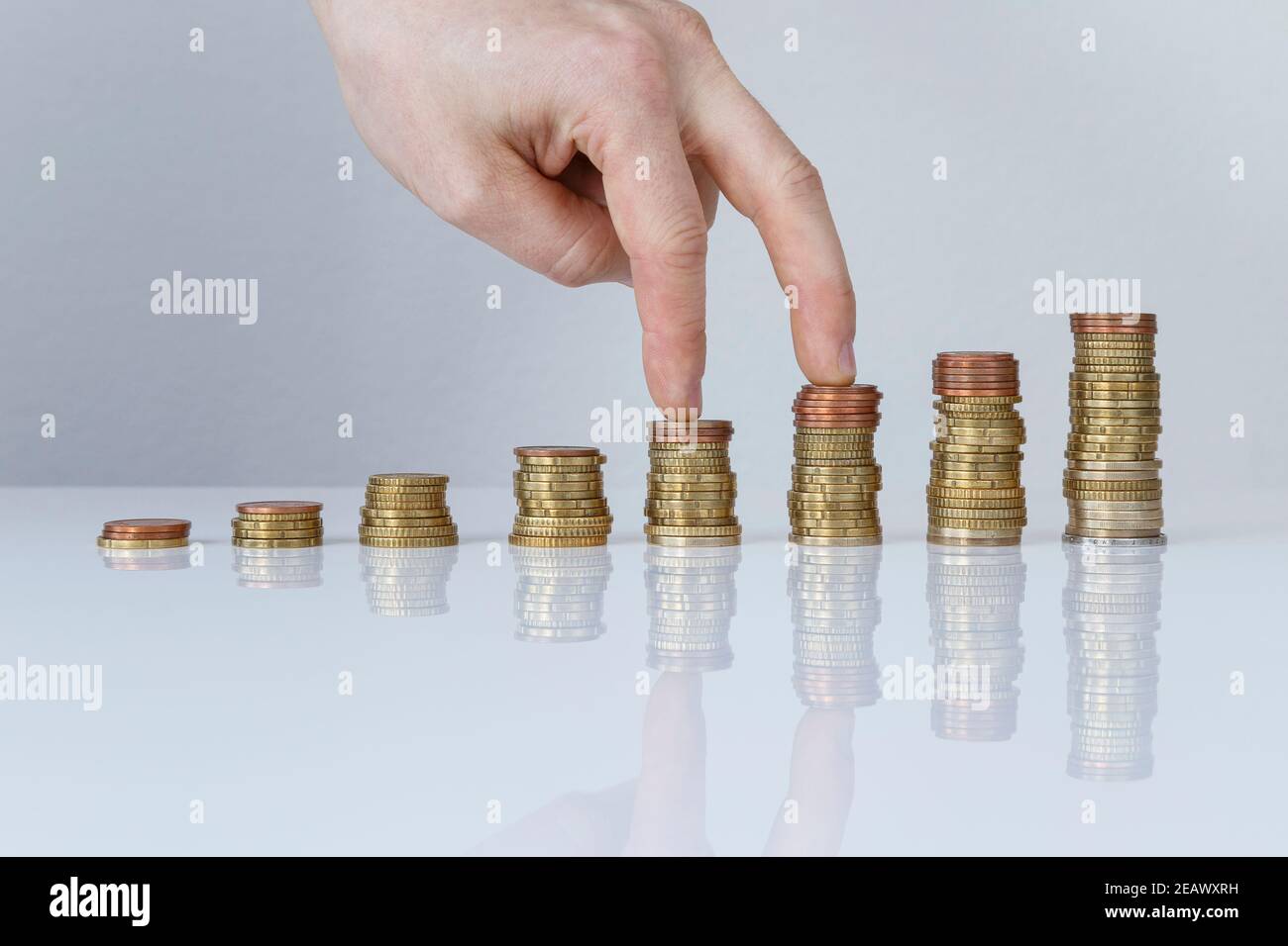 Hand on ascending stacks of coins against gray background. Concept photo of earning, home and personal finances, financial goals and growth. Stock Photo