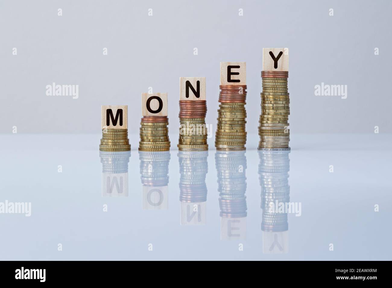 Word MONEY on wooden blocks on top of ascending stacks of coins on gray background. Concept photo of making money, earning, economy, financial growth. Stock Photo