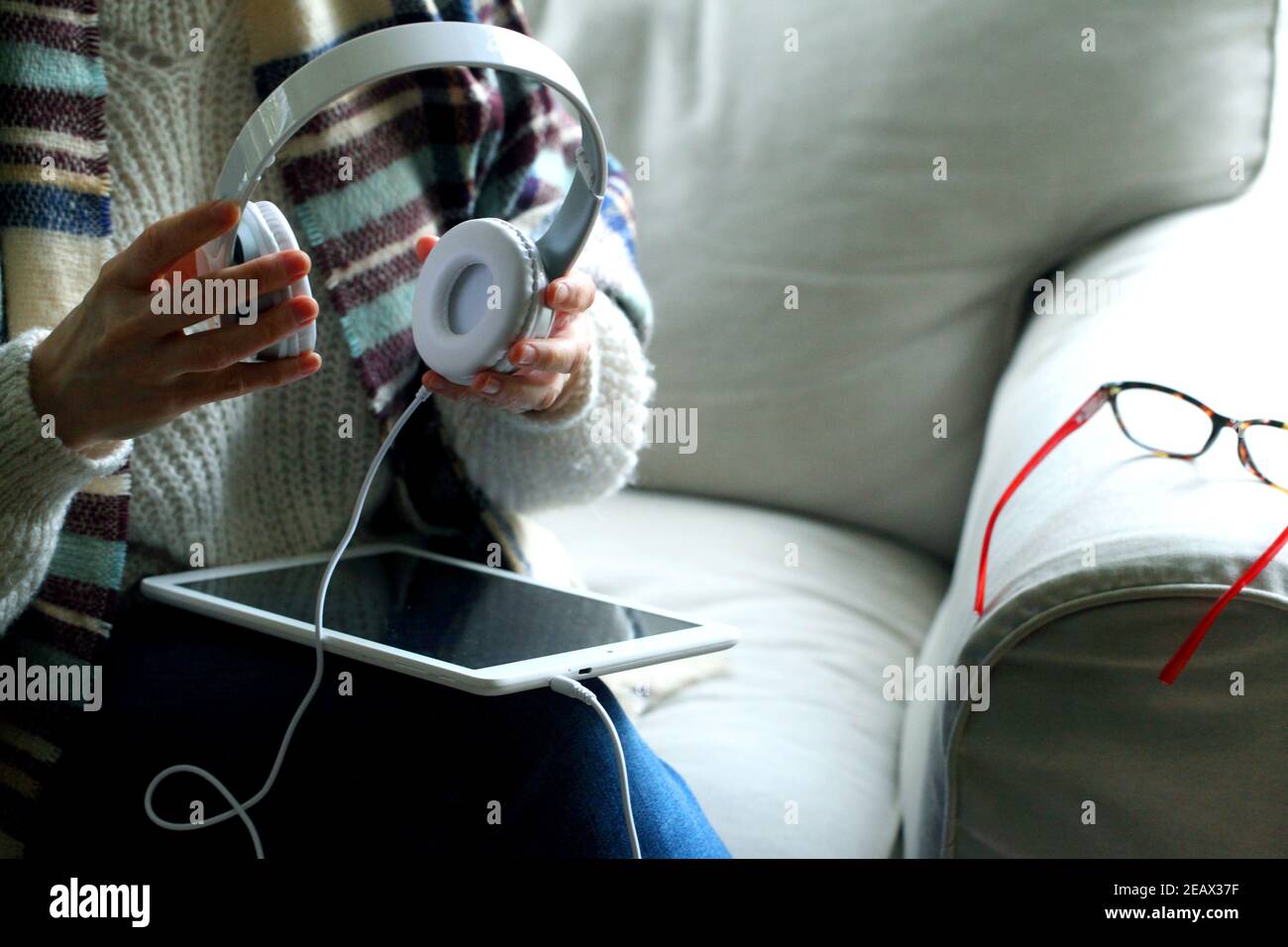 Closeup shot of a woman sitting on the couch holding a tablet and headphones Stock Photo