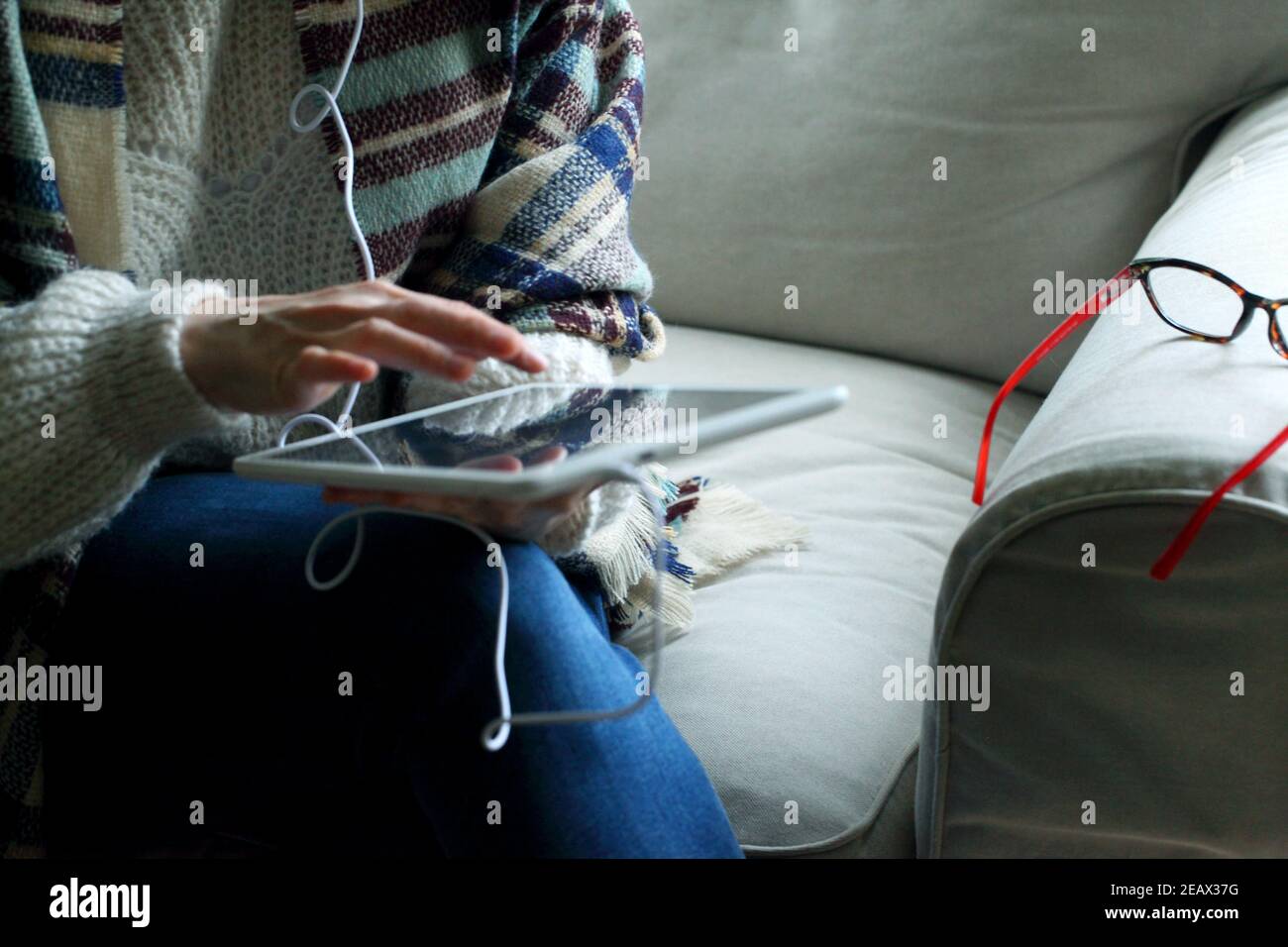 Closeup shot of a woman sitting on the couch holding a tablet Stock Photo