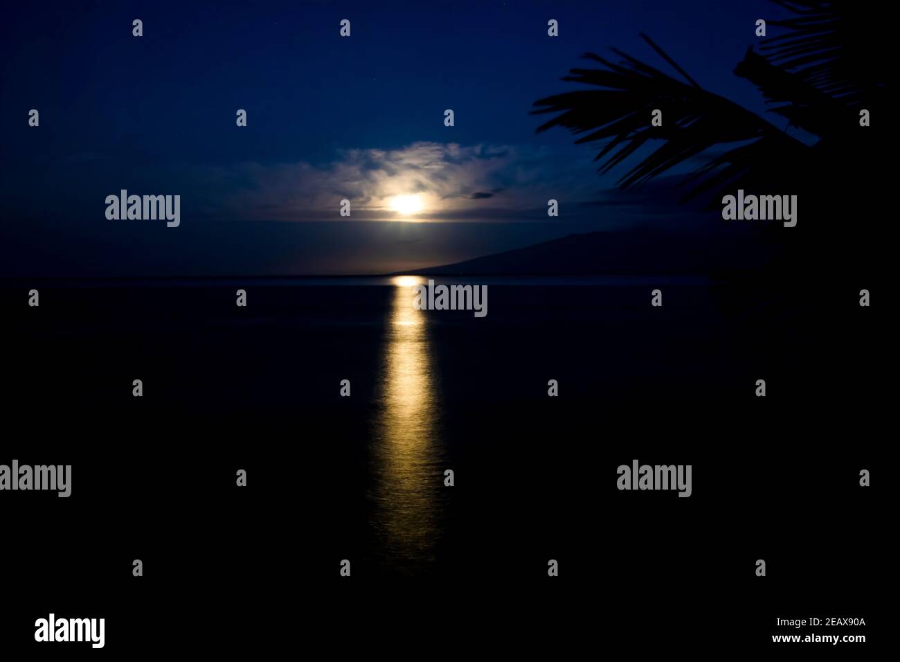 Full moon setting through clouds and reflecting on surface of the sea in tropical Hawaii. Stock Photo
