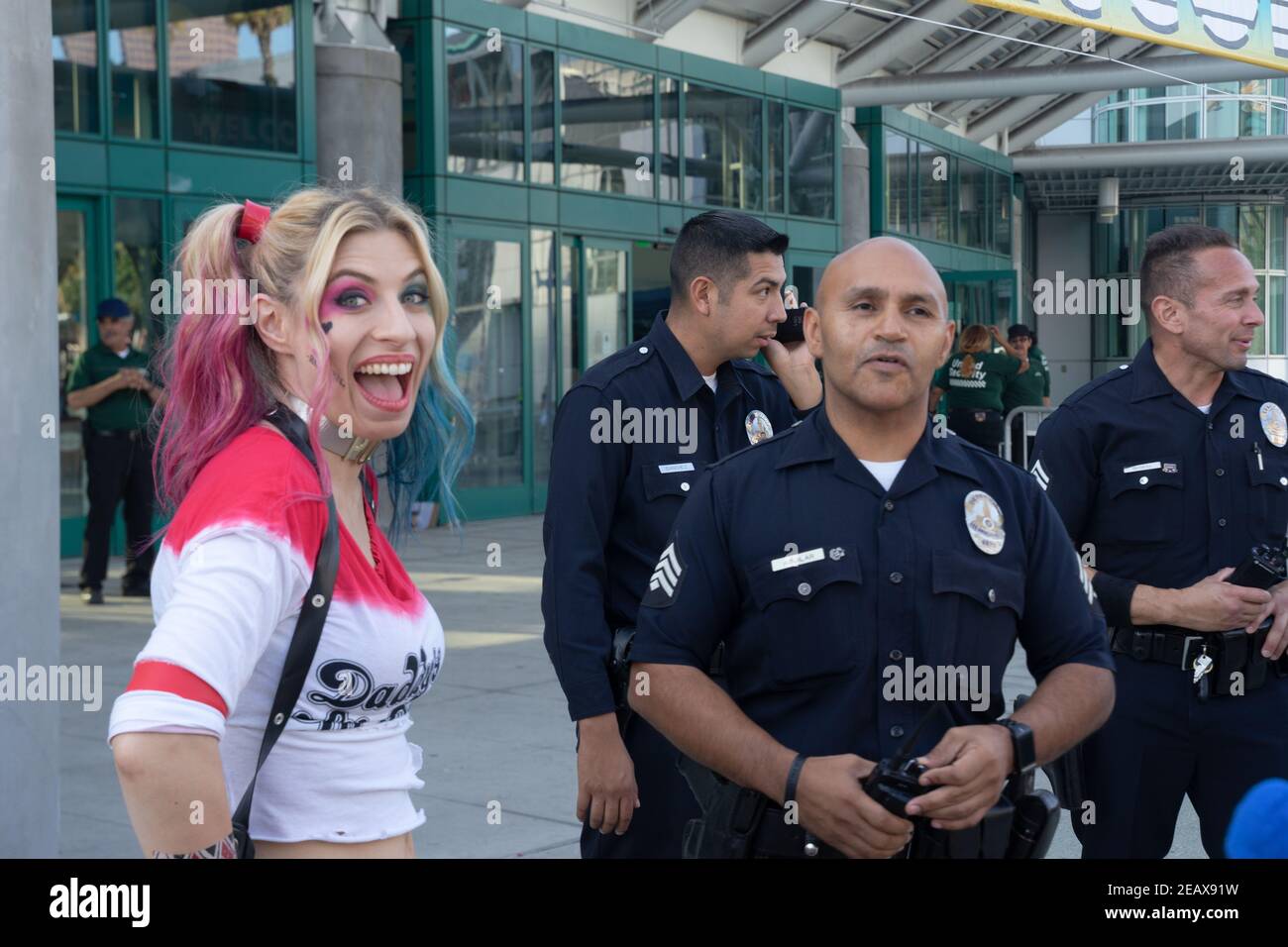 A cosplayer dressed as Harley Quinn from the DC universe poses smiling widely next to three LAPD policemen on duty. Stock Photo