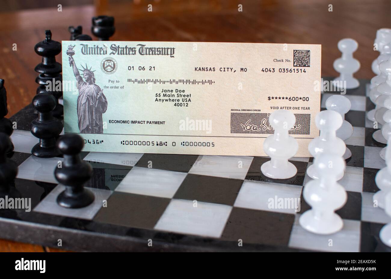A stimulus check sits on A carved chess set, and illustrates the concept of republicans vs the democrats in the fight for government aid during Stock Photo