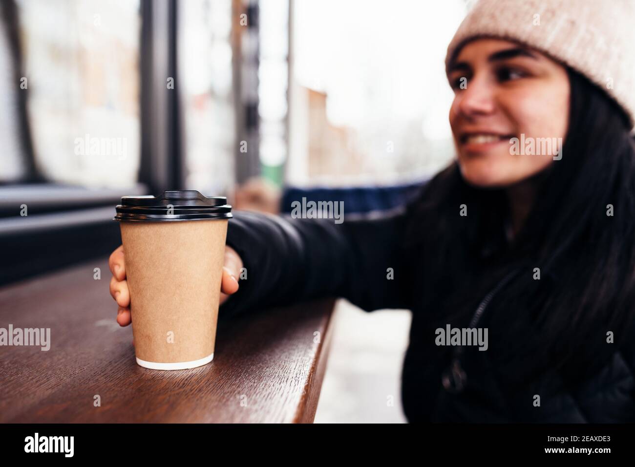 Girl smiling, holds paper cup of coffee in hand near cafe. Blurred background. High quality photo Stock Photo