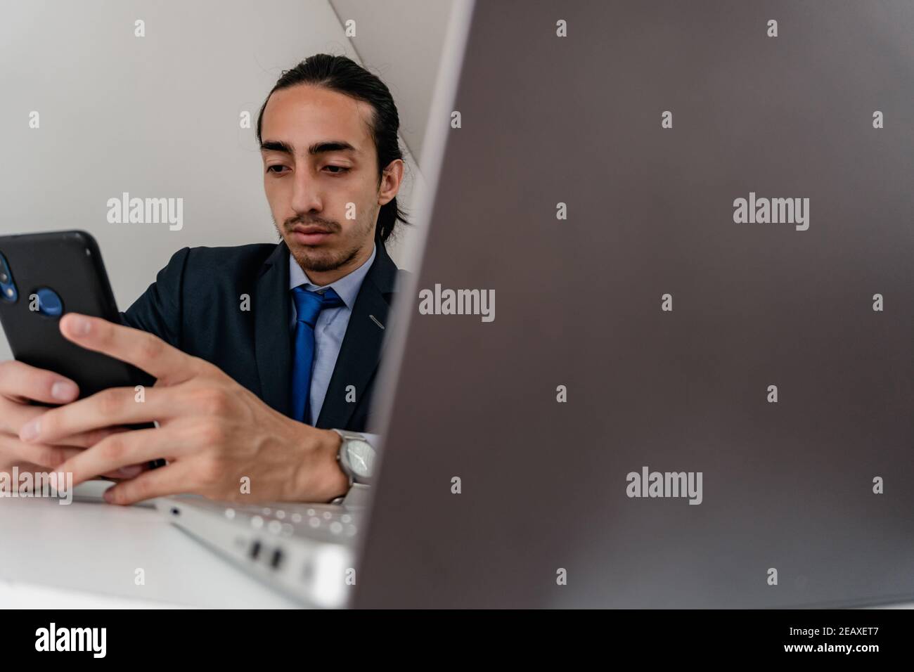 hidden camera captures young businessman working on cell phone and computer, wearing monochromatic blue suit, workday Stock Photo
