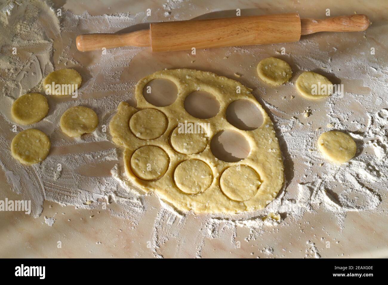 Making curd biscuits. Rolled dough and round raw biscuits on wheat flour near rolling pin Stock Photo