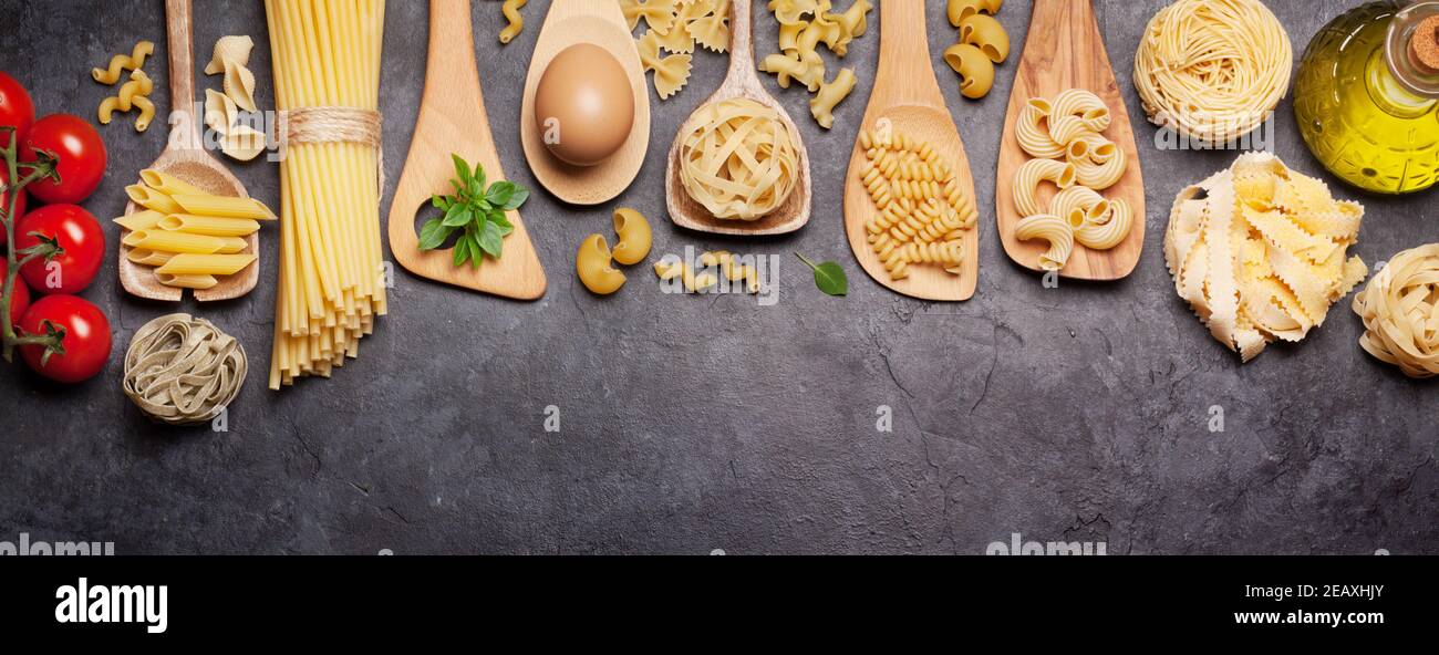 Various pasta in spoons, tomatoes and olive oil. Top view flat lay Stock Photo