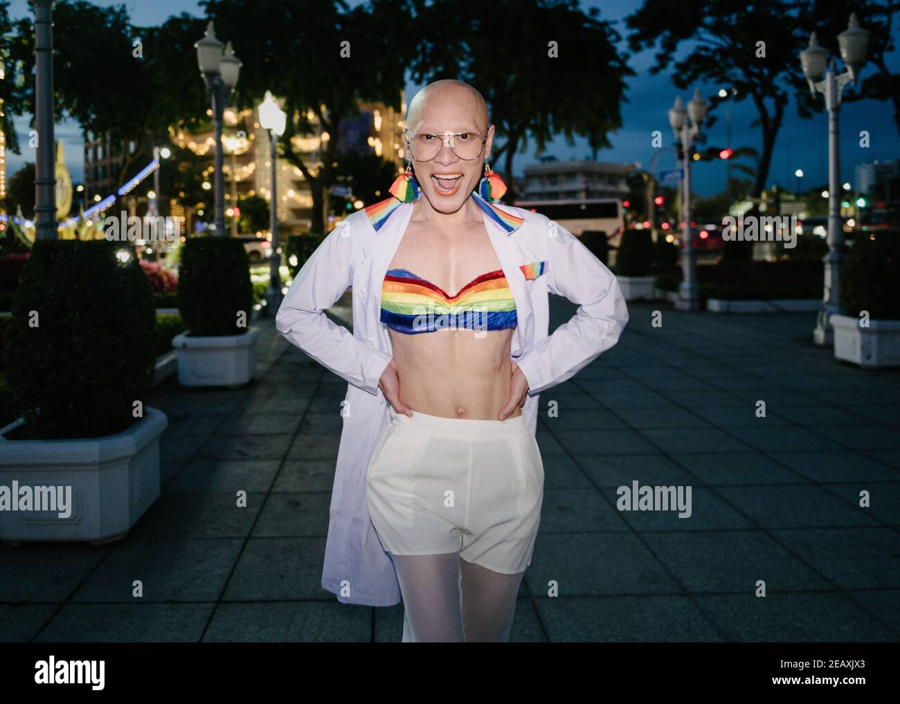 An Asian Queer person wearing a medical doctor white uniform with rainbow colors items to protest against discrimination of LGBTQ community members. Stock Photo