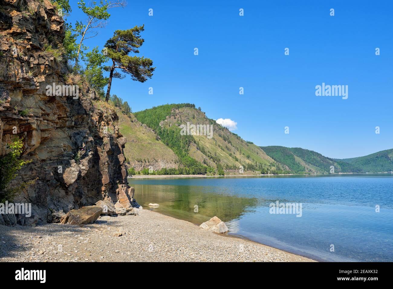 Baikal landscape on a sunny summer day. A pine tree leaned over the edge of the cliff above the water. Irkutsk region. Russia Stock Photo