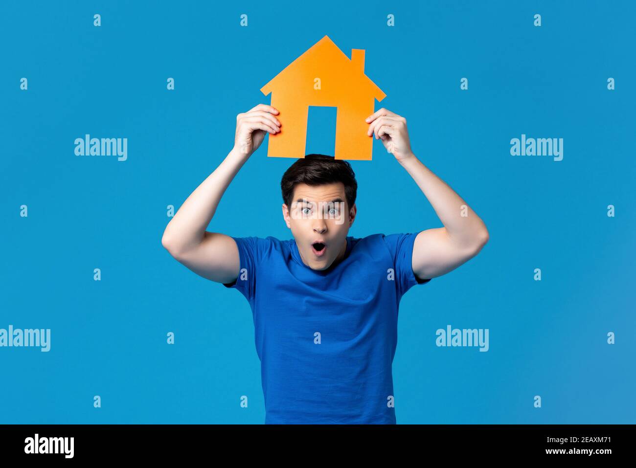 Excited handsome caucasian man holding a housing model overhead isolated on blue studio background Stock Photo