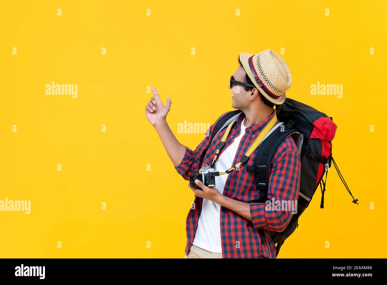 Happy Asian man tourist backpacker pointing hand to copy space aside  isolated on yellow studio background Stock Photo