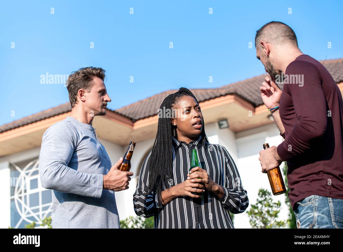 Group of diverse friends drinking alcohol and talking outdoors in backyard Stock Photo