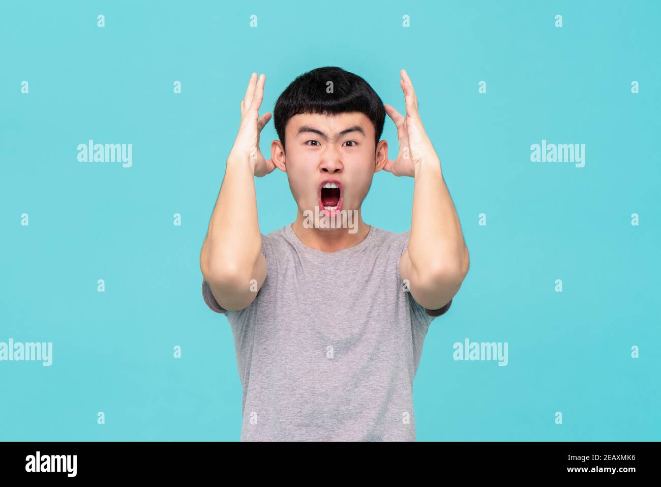 Aggressive angry young Asian man emotionally shouting isolated on light blue studio background Stock Photo