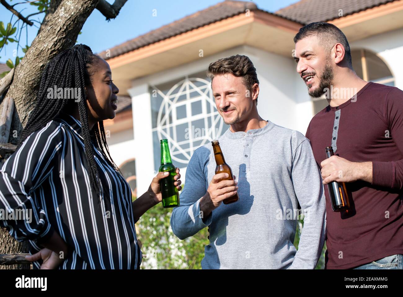Gay couple and African American woman friend enjoying chatting and drinking alcohol outdoors at the house on weekend Stock Photo