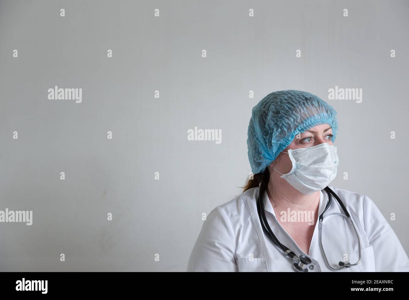 Image of a tired paramedic woman in medical clothes against a white wall looking to the side her gaze is fixed. Stock Photo