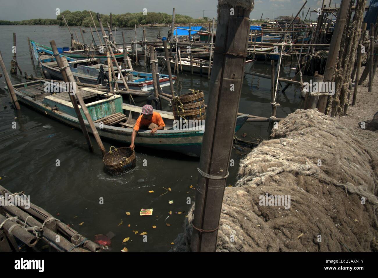 A worker washing rattan baskets on sea water from a boat tied to the landing beach of Kamal Muara, a fishing village also known as a green mussel production center in the coastal area of Jakarta, Indonesia. Stock Photo