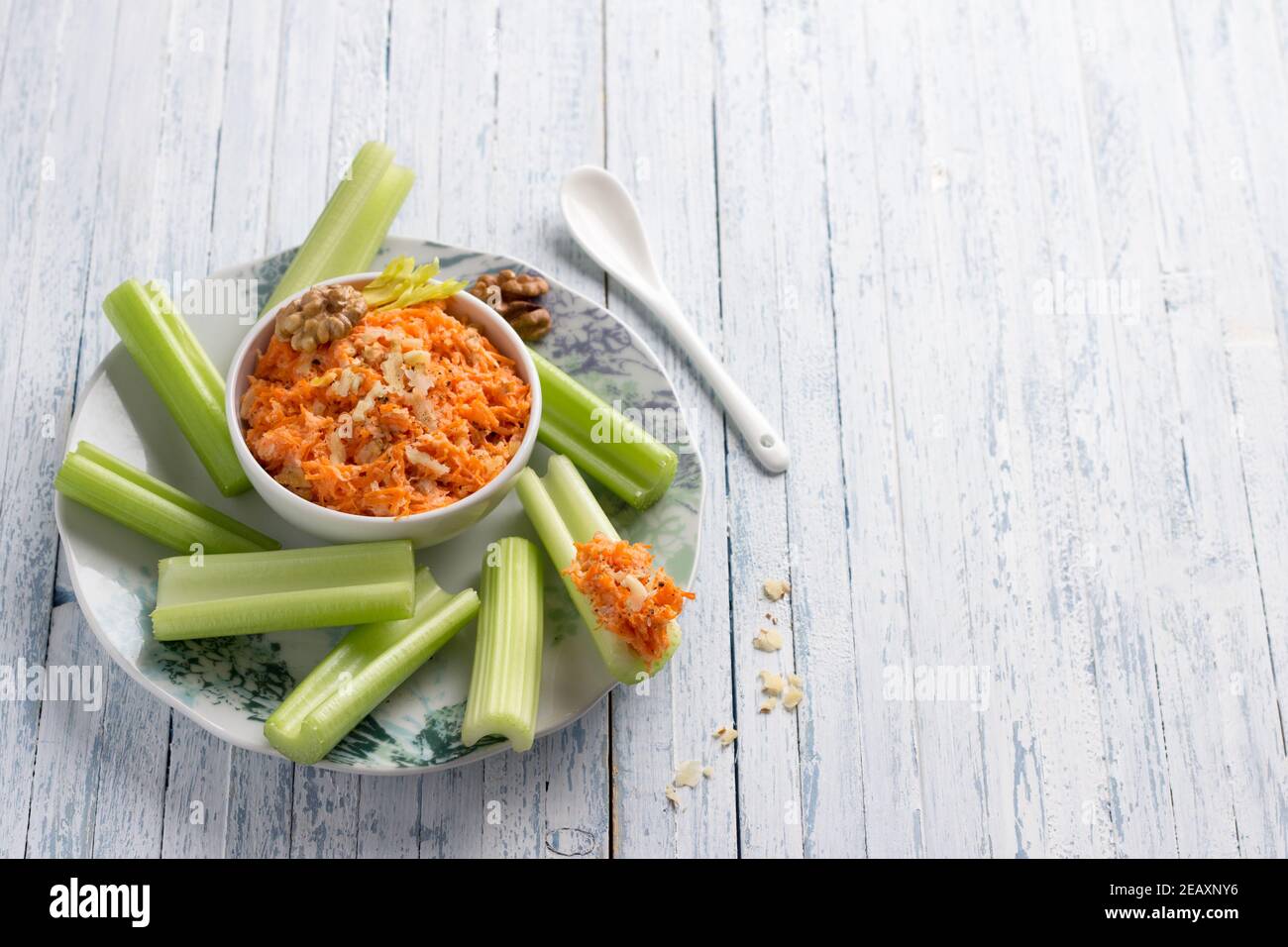 Delicious vegetable diet snack, celery stalks with carrot dip with nuts, garlic, spices and yoghurt dressing on light blue background, top view, selec Stock Photo