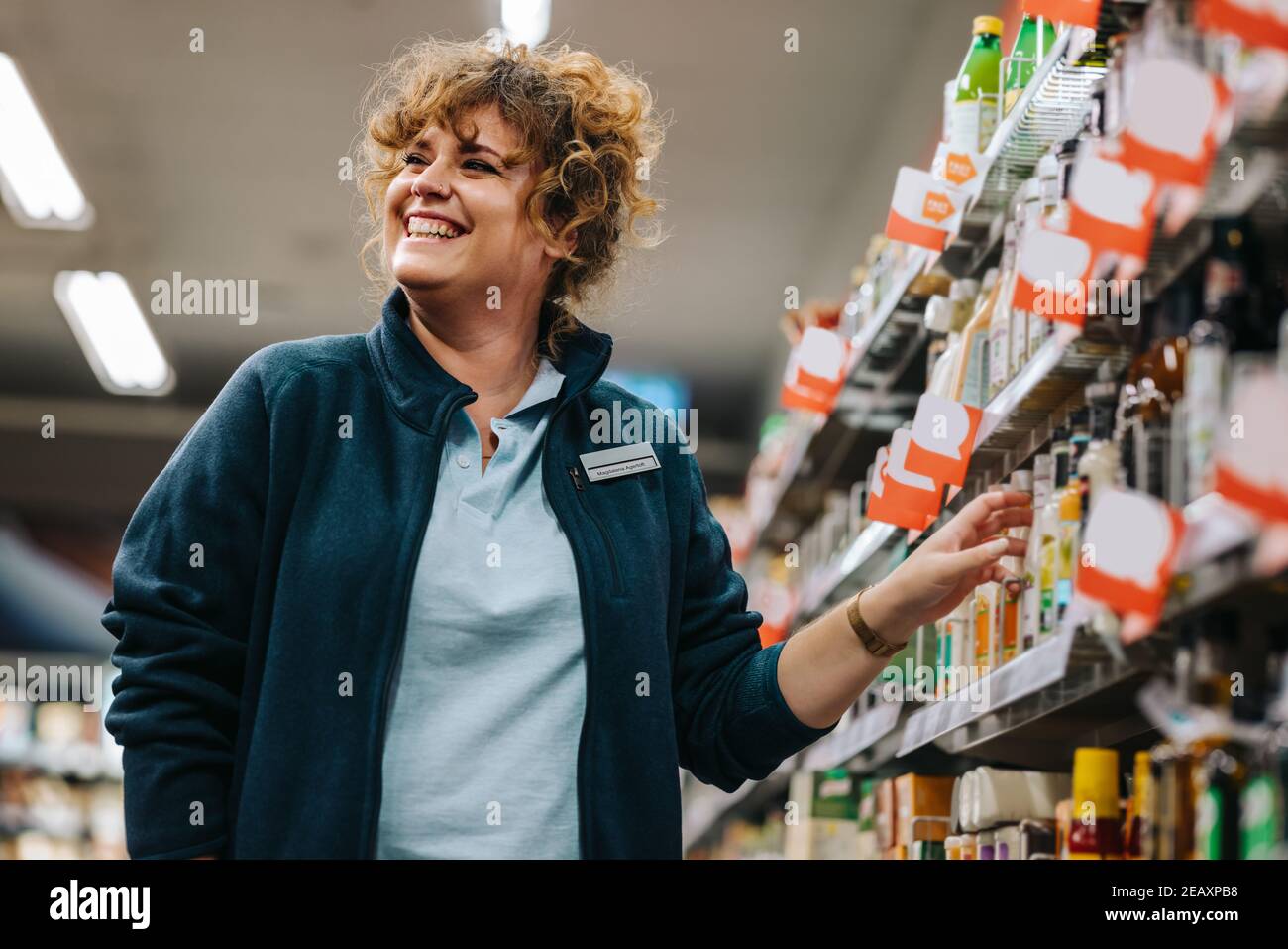 Confident businesswoman standing by the shelves and smiling in supermarket. Female manager at a grocery store. Stock Photo