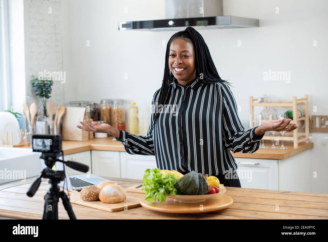 Happy African American woman vlogger broadcasting live video online teaching cooking food in kitchen at home Stock Photo