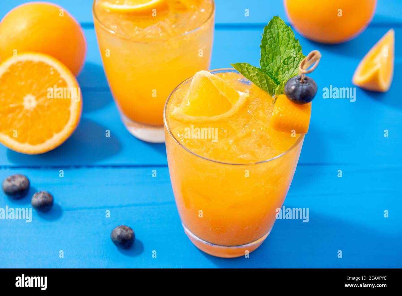 Fresh fruit juice mocktail drinks in the glasses with oranges and blueberries on colorful blue table Stock Photo