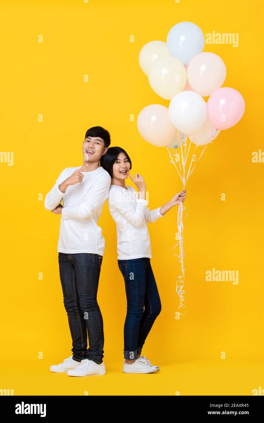 Attractive cheerful young Asian lover happily holding colourful ballons on yellow studio background Stock Photo