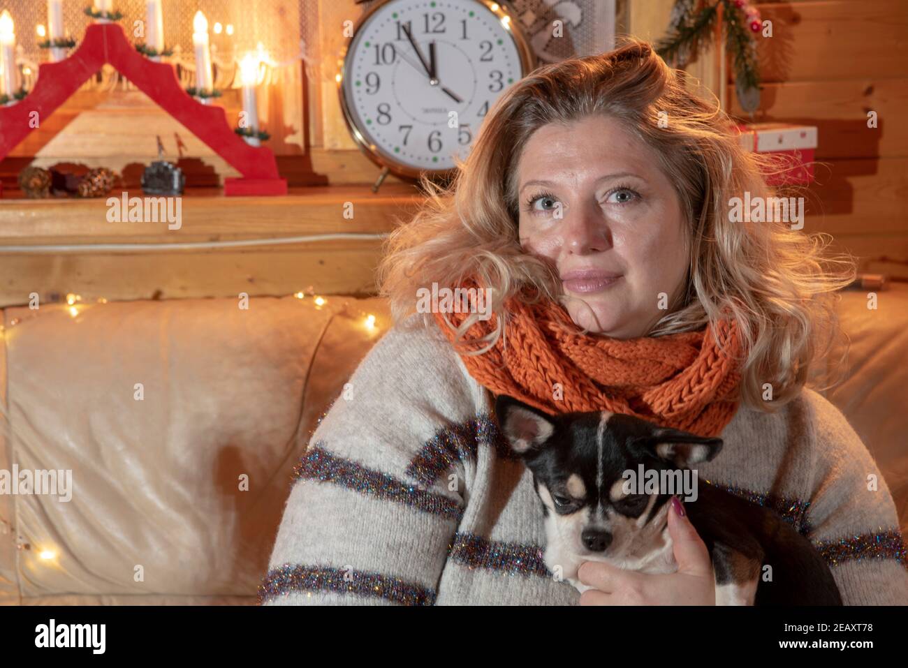 Portrait of a plump, middle-aged blonde woman sitting on a sofa with a Chihuahua . Stock Photo
