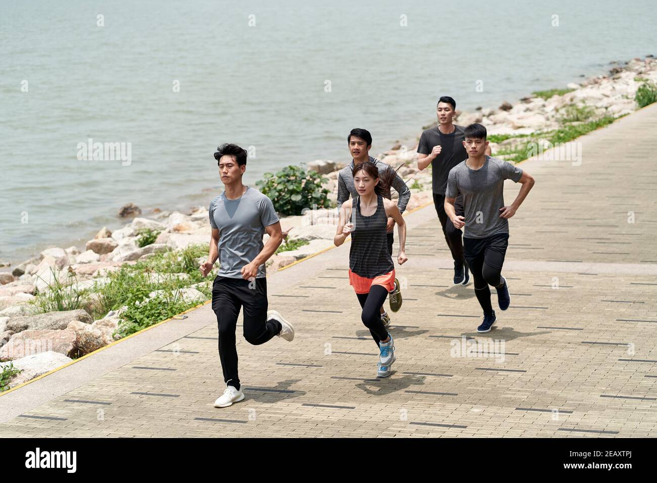 group of five young asian adults running outdoors in seaside park Stock Photo