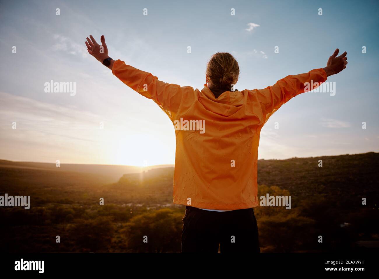 Rear view of young man standing on mountain with outstretched arms feeling relaxed after morning running in nature Stock Photo