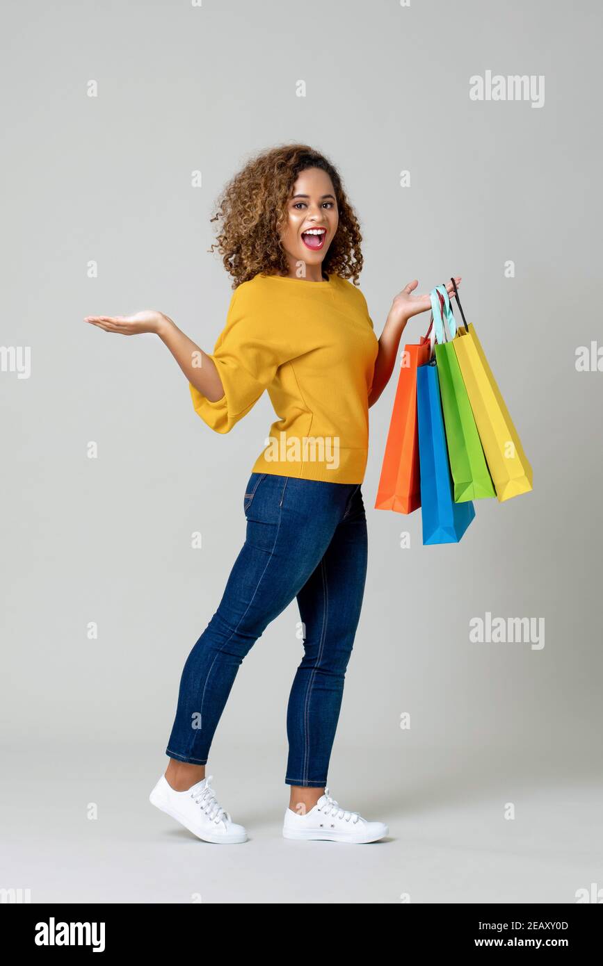 Young African American  woman holding colorful shopping bags with another hand open on light gray background Stock Photo