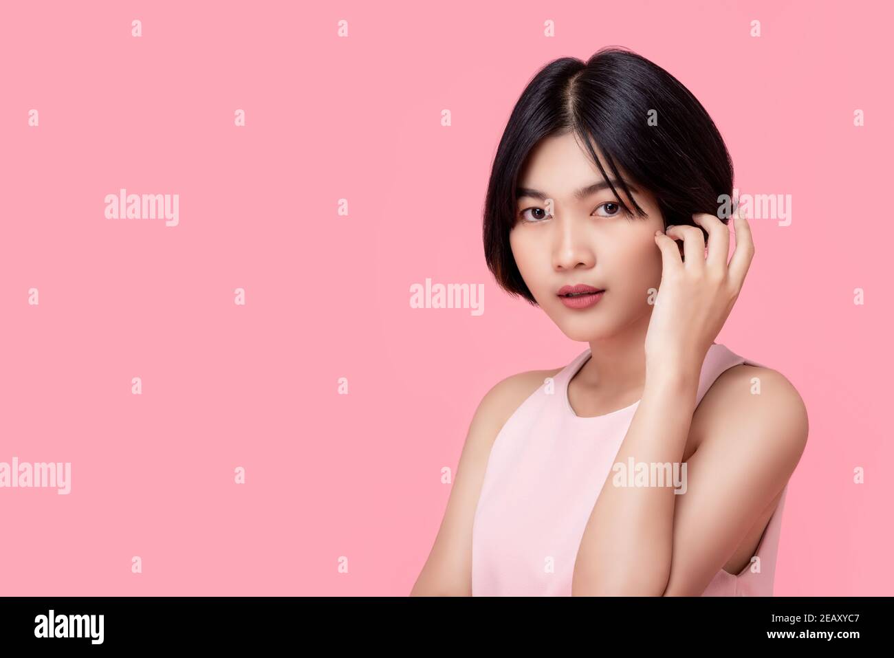 Young short hair discreet Asian woman model wearing sleeveless blouse looking at camera isolated in pink studio backgound with copy space Stock Photo