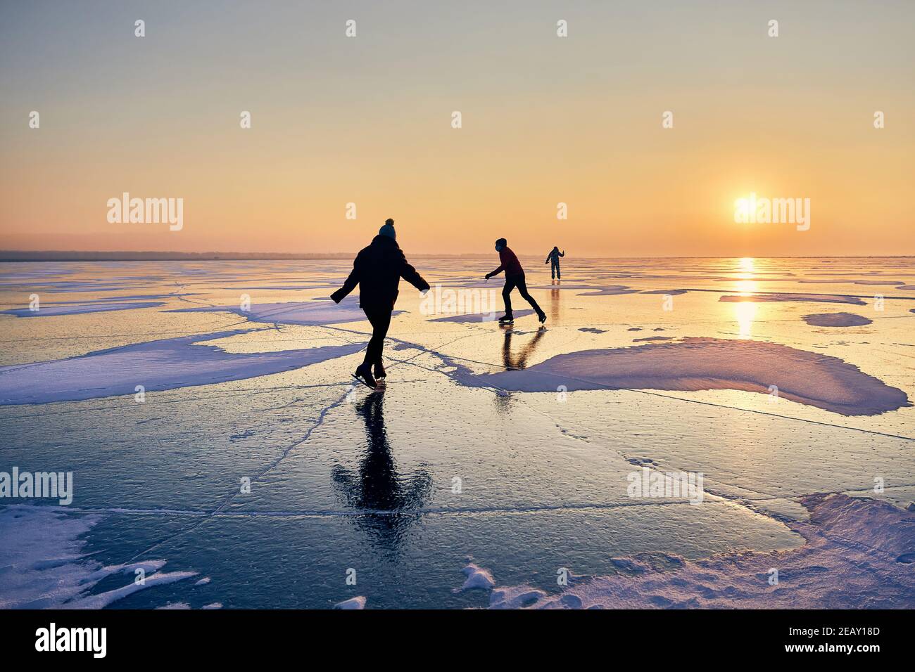 People are ice skating in silhouette at frozen lake against beautiful orange sunrise Stock Photo
