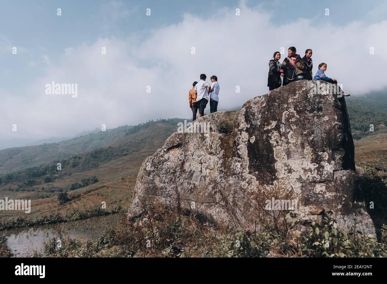 H'mong hill tribe people standing on top of a cliff in an open field surrounded by green hills with blue sky and white clouds. Stock Photo