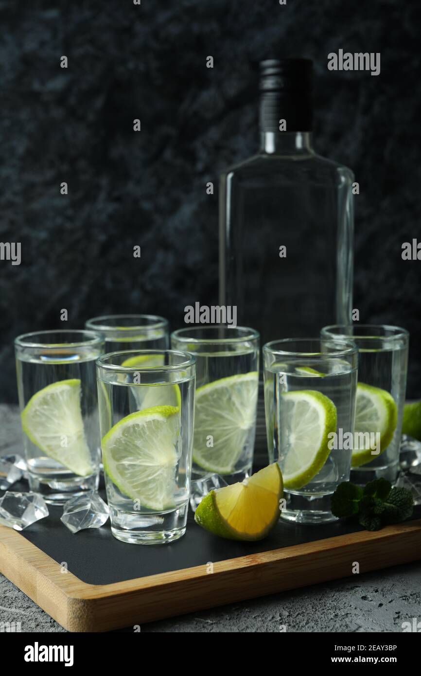 Board with bottle and shots of vodka with lime on gray table Stock