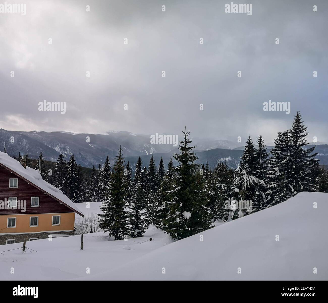 Winter view overlooking a lodge in the mountains surrounded by evergreens and snow on a cloudy day, in Ranca resort, Romania Stock Photo
