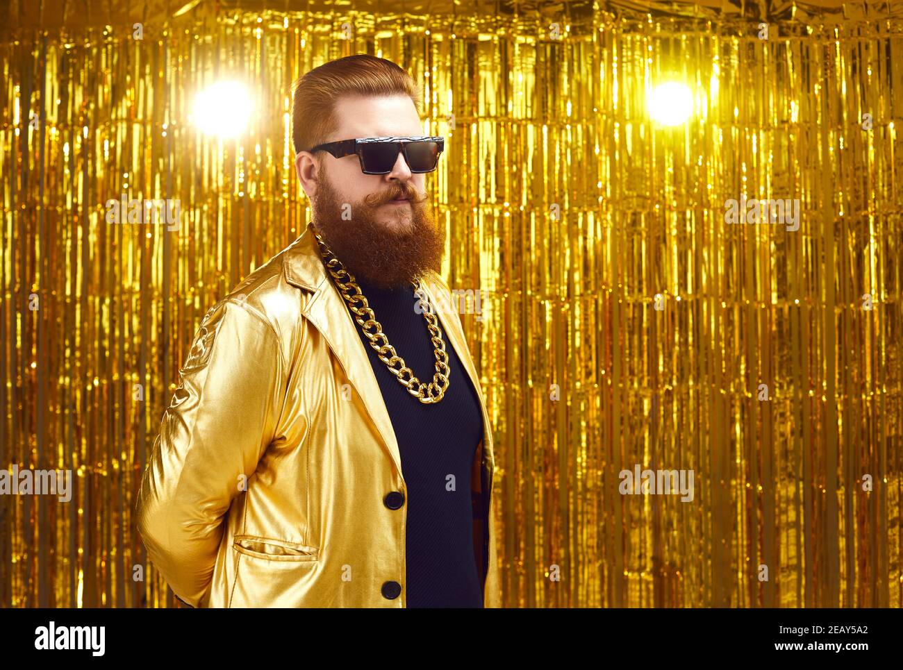 Comically serious cool bearded man in sunglasses stands on a golden background. Stock Photo