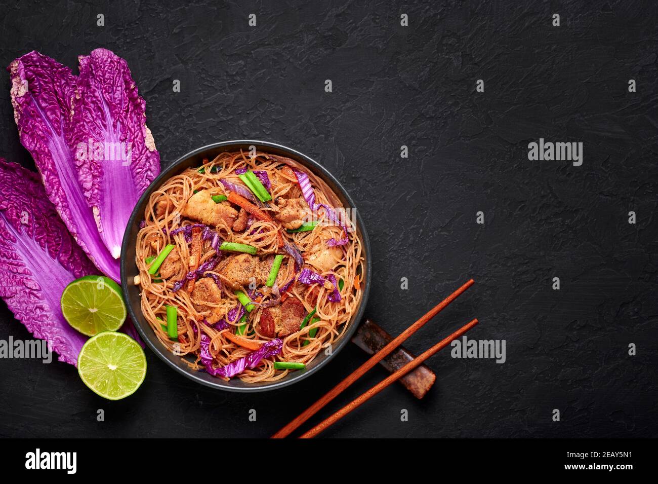 Pancit Bihon in black bowl on dark slate table top. Filipino cuisine noodles dish with pork belly, chicken, vegetables. Asian food. Top view. Copy spa Stock Photo
