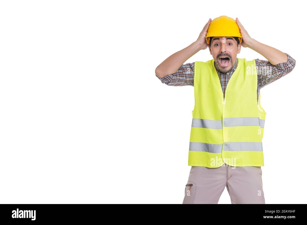 Shocked male builder in reflective vest standing on white background and touching hardhat while looking at camera in astonishment Stock Photo