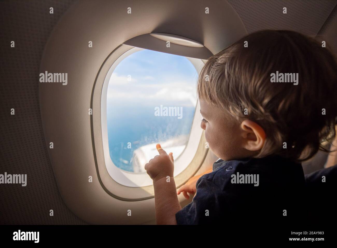 Toddler looks at the ground through the porthole of a flying plane. travel with children Stock Photo