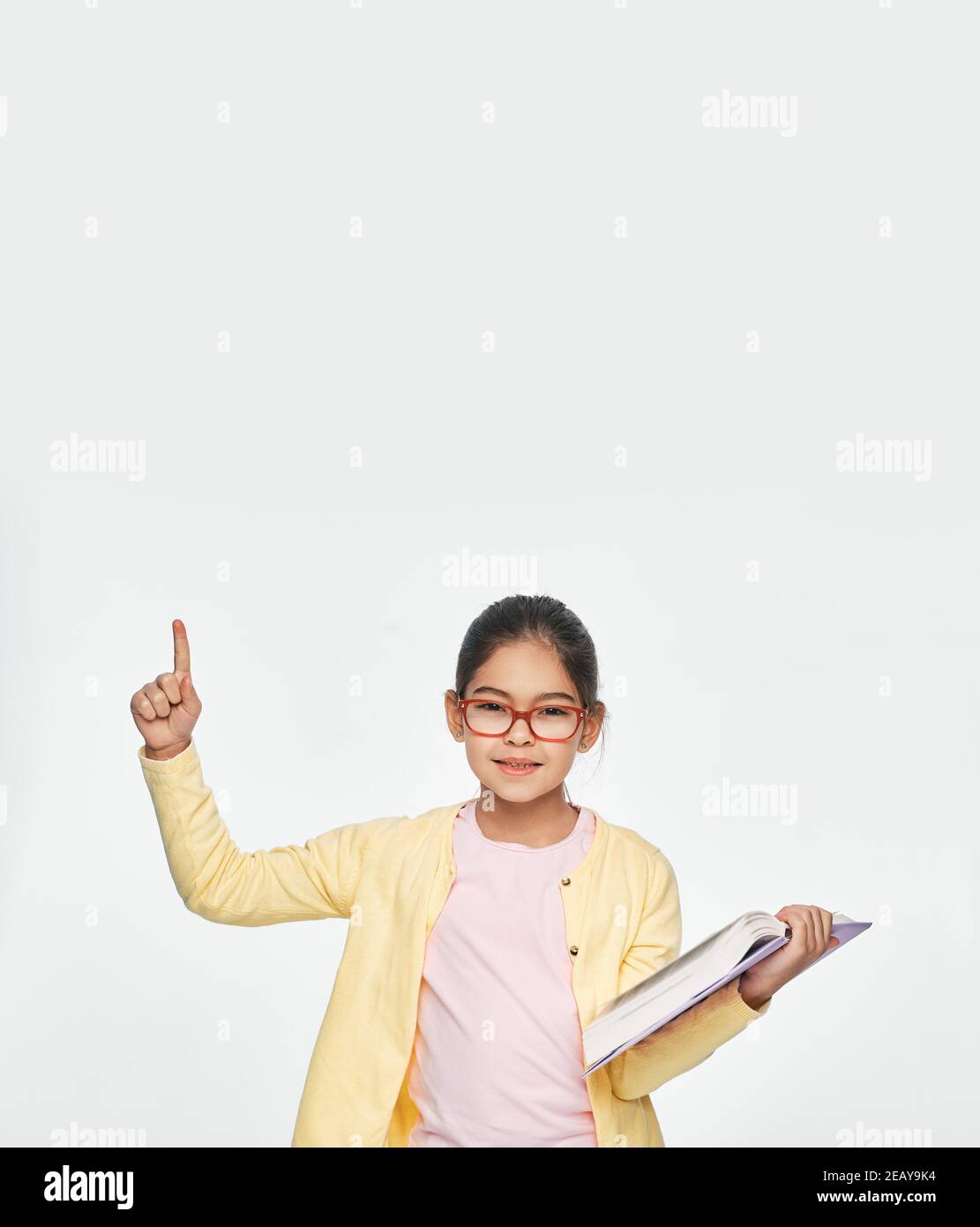 Asian child with book in hands shows index finger up, isolated on light gray background Stock Photo