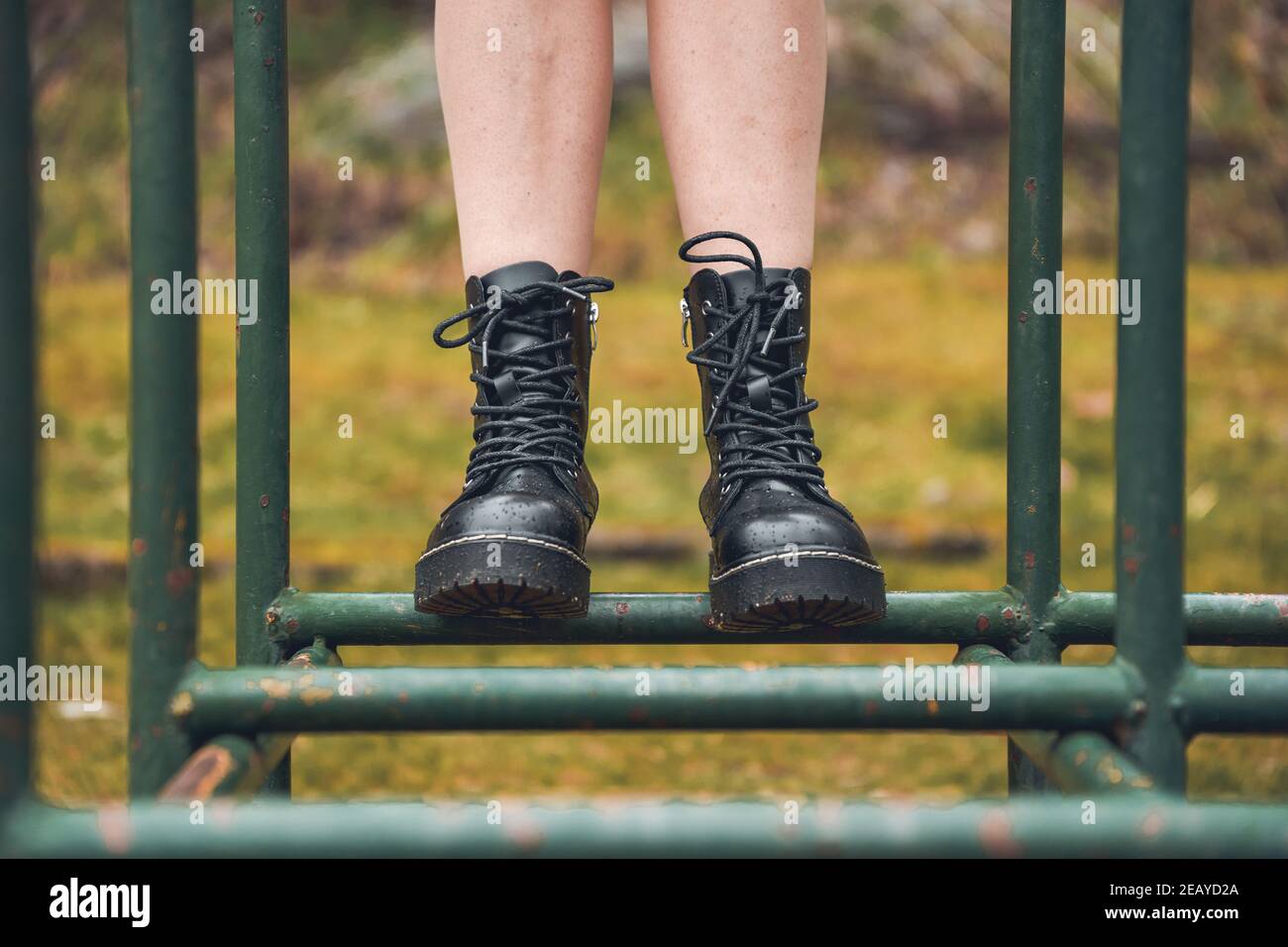 Lady wearing black ankle boots standing on a metallic structure in a park Stock Photo